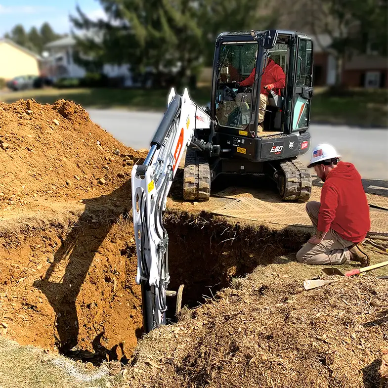 two plumbers digging a sewer line with an excavator